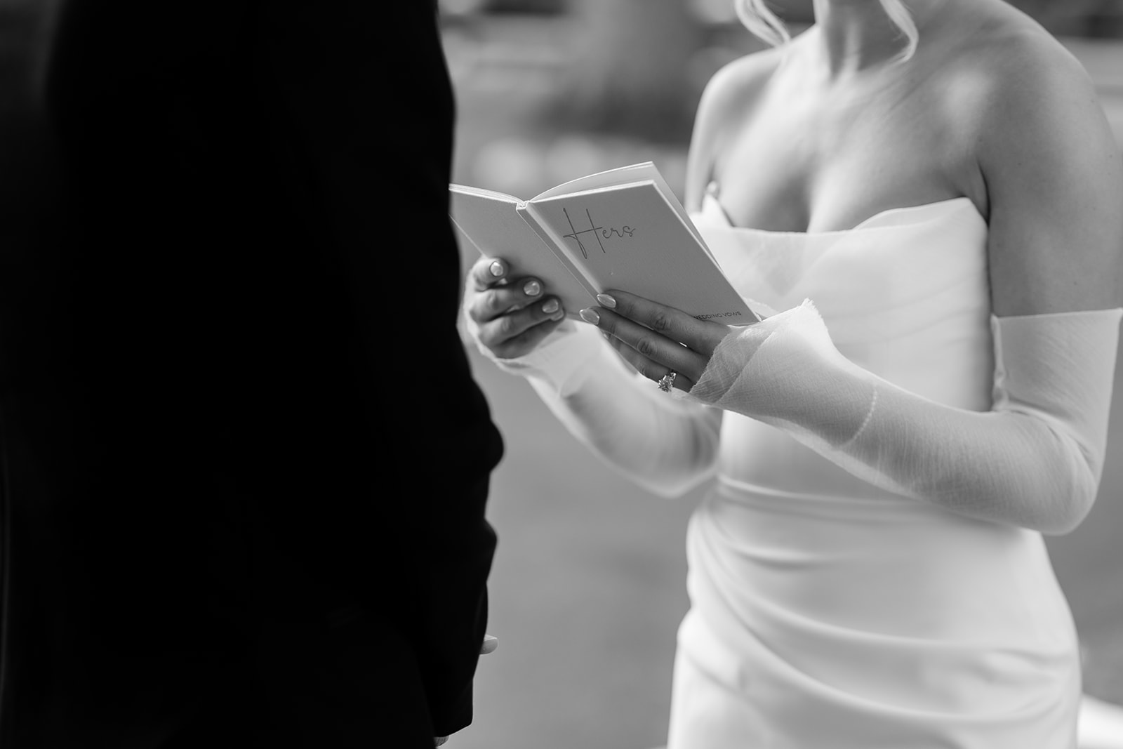 Black and white close-up of the bride holding her vow book and reading to the groom during the ceremony.